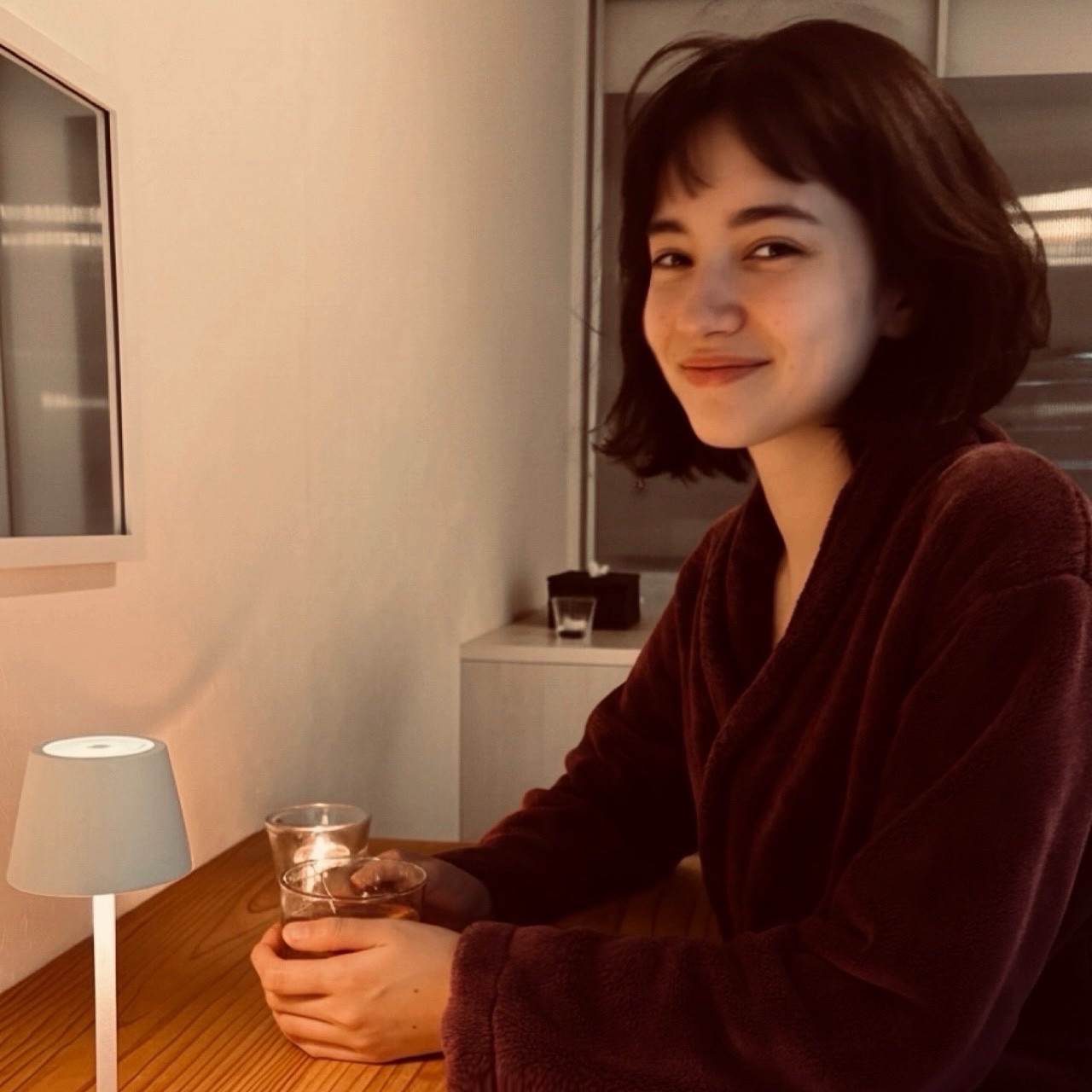 MoonTed Diary: A smiling woman with a bob haircut, in a maroon gown, holding a glass at a table lit by a white lamp