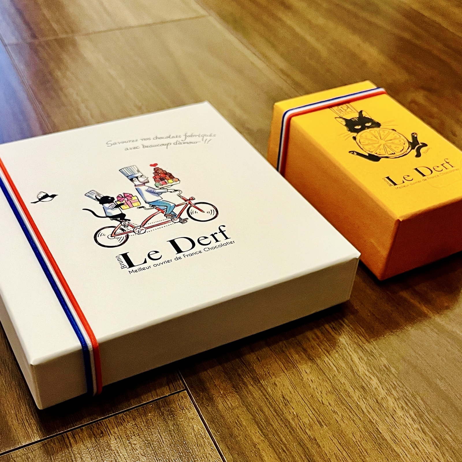 ムーンテッド(MoonTed)の日記より、ル・デルフ(Le Derf)のチョコレートの箱2つ。自転車に乗るシェフのイラストの白い箱と、猫のイラストの黄色い箱