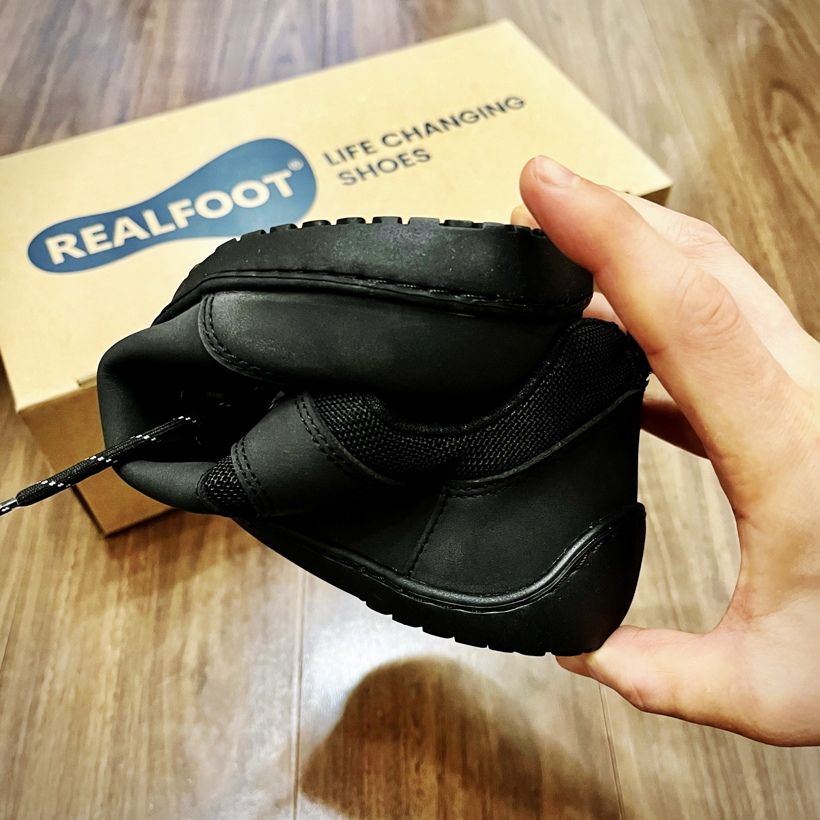 ムーンテッド（MoonTed）の日記より、手で曲げたRealfootの黒いベアフットシューズ。奥に「LIFE CHANGING SHOES」と書かれた箱
