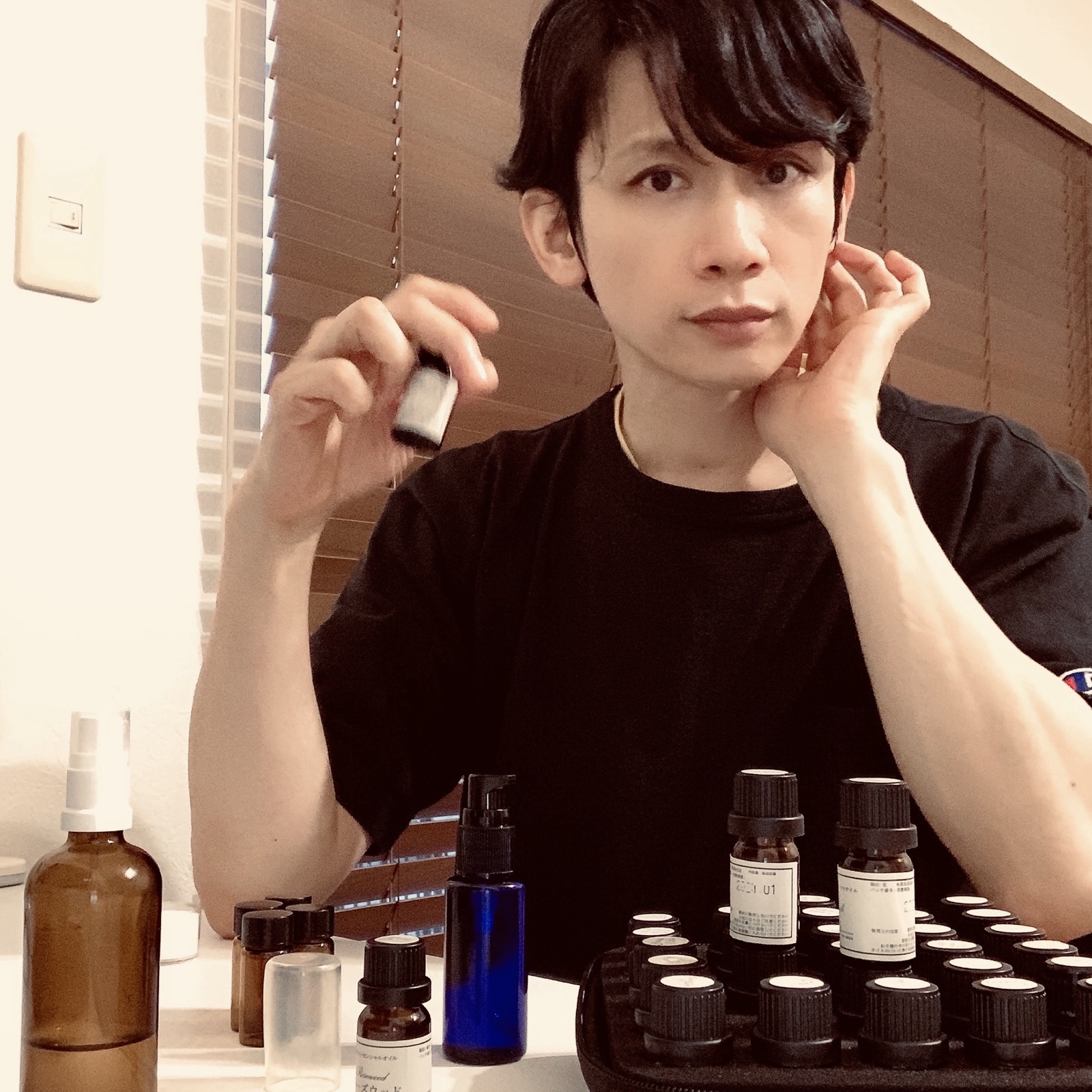 ムーンテッド(MoonTed)の日記より、精油の小瓶を手に、頬に手をあてるムーンテッド(MoonTed)のセラピストAKI。手前に並ぶたくさんの精油