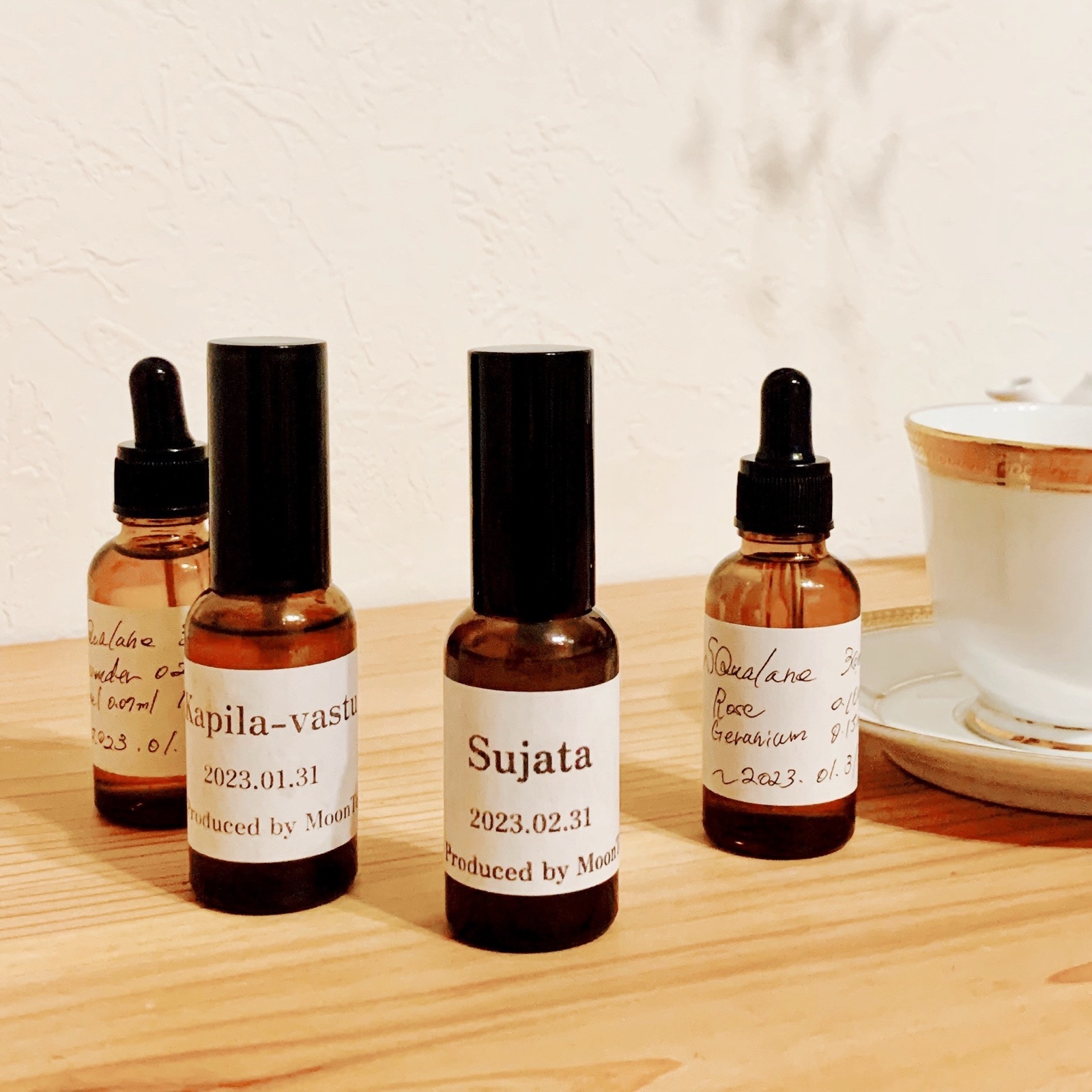ムーンテッド(MoonTed)の日記より、「Sujata」と「Kapila-vastu」のラベルの香水瓶。手前にスクワランオイルのスポイト瓶、奥にティーカップ