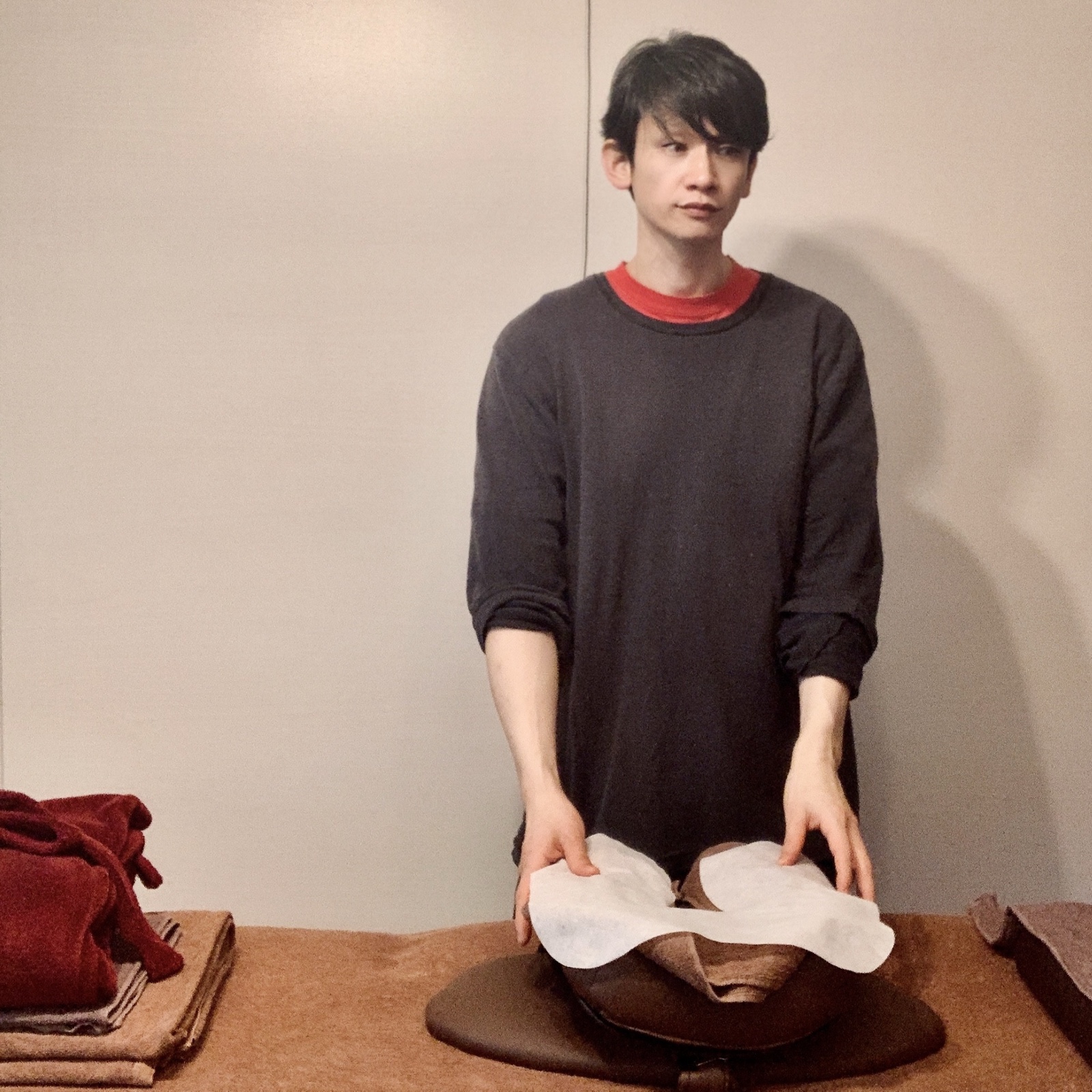 ムーンテッド(MoonTed)の日記より、施術台の穴枕に紙のフェイスカバーを敷くムーンテッド(MoonTed)のセラピストAKI。こげ茶のニット姿