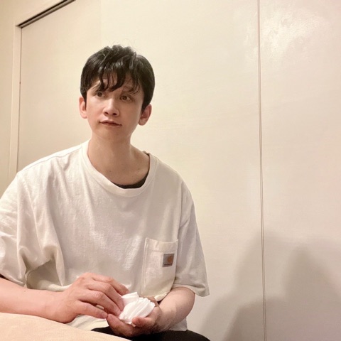 ムーンテッド（MoonTed）の日記より、施術台の横に座り、手に白い布を持つムーンテッド（MoonTed）のセラピストAKI。白いTシャツ姿