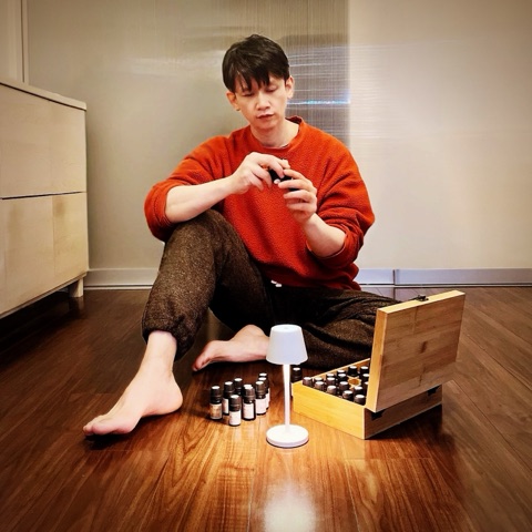 MoonTed Diary: Therapist AKI sitting barefoot on the floor with a small essential oil bottle, oils in a wooden box and a white lamp in front